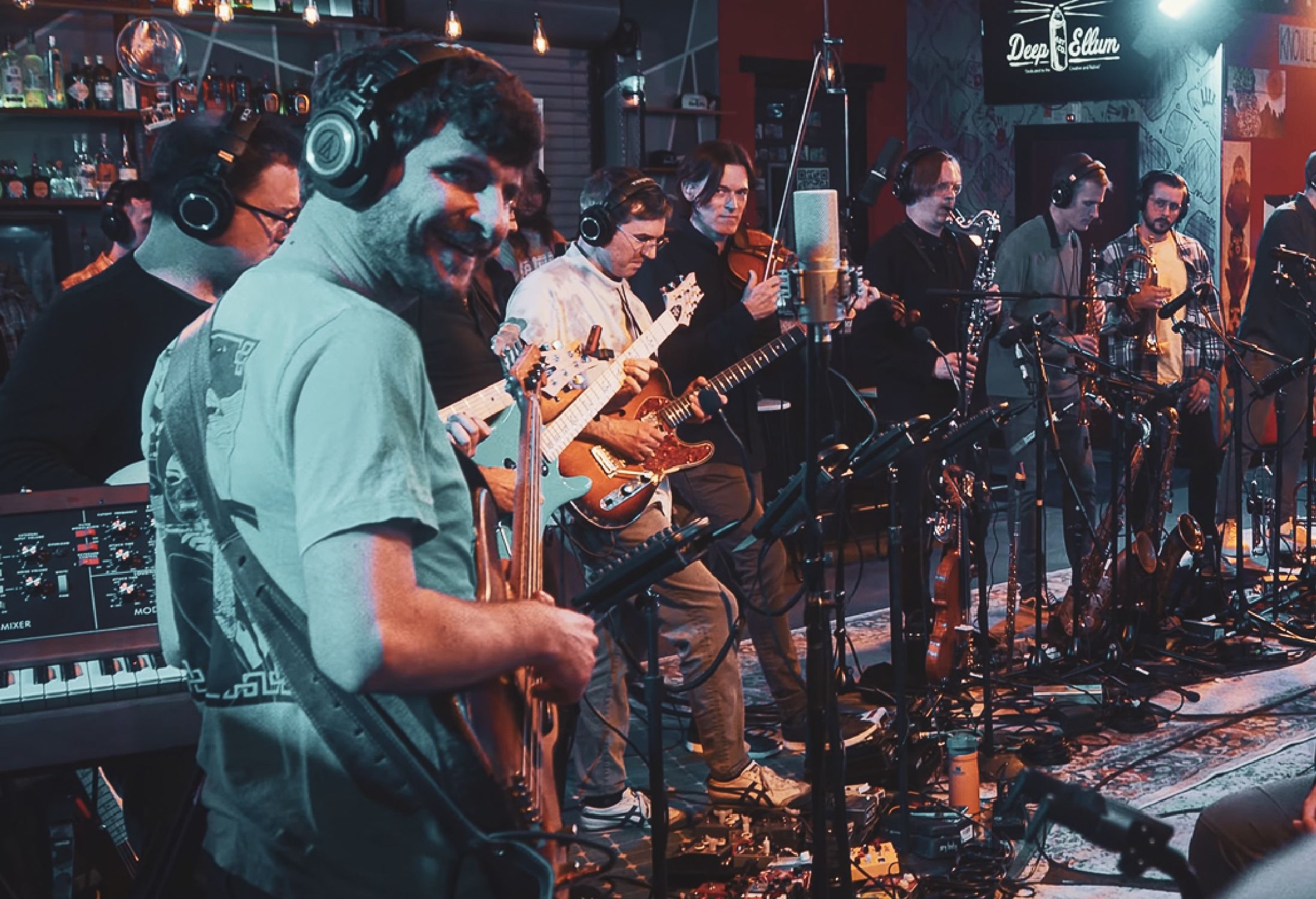 A bass player smiling while performing in a band with many musicians
